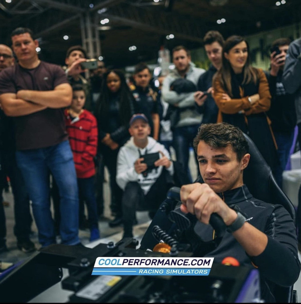 Lando Norris driving a Cool Performance Formula Pro simulator in front of a crowd