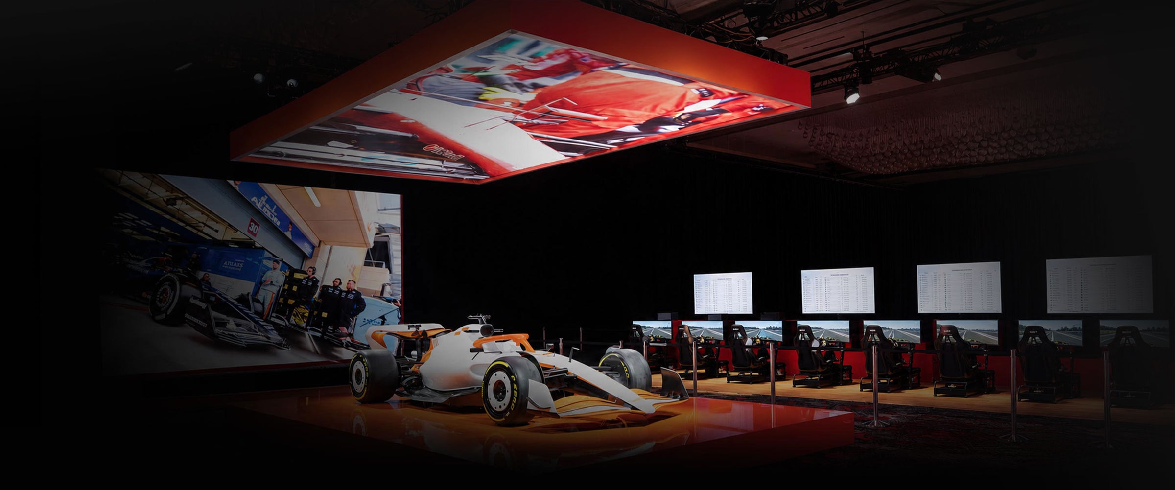 A Formula 1 race car displayed in a convention hall, with multiple racing simulators and large leaderboard screens in the background under dramatic overhead lighting. All supplied by Cool Performance simulator rental